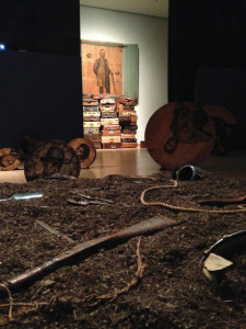Whitfield Lovell (b. 1959); Deep River, 2013; 56 wood discs, found objects, soil, video projections and sound; size variable; and Flight, 2013; Wood cabinet, suitcases, music stand, chest, sheet music, chains, rope. Courtesy of the artist and DC Moore Gallery, New York.